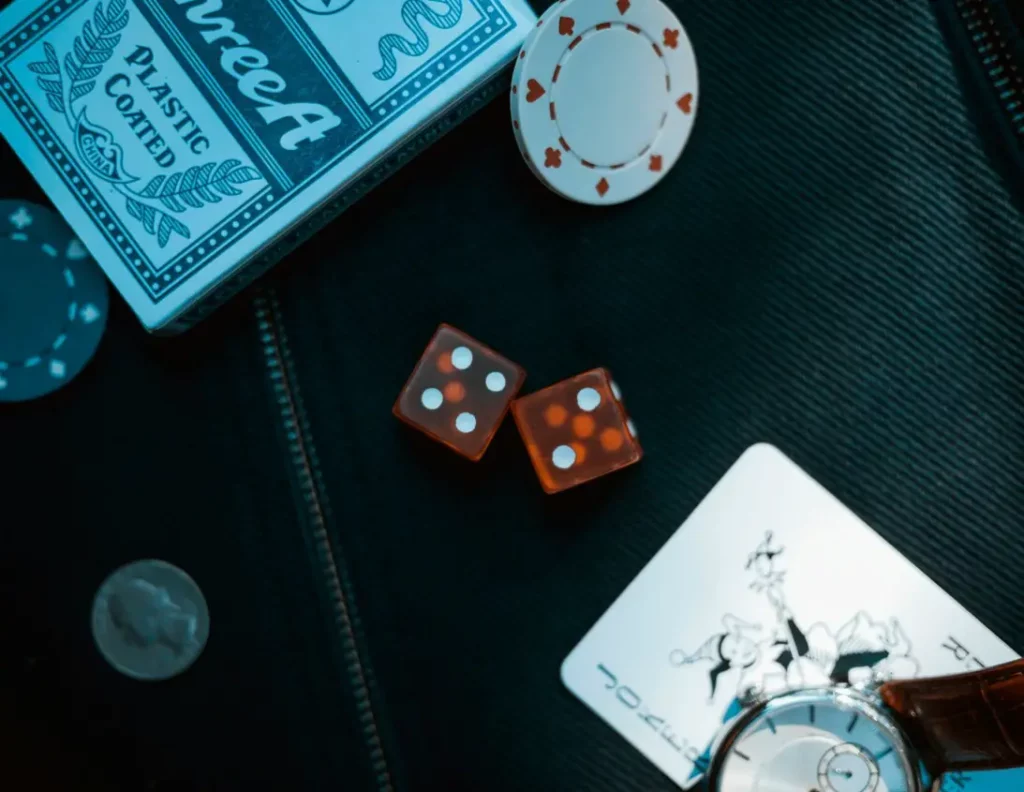 Assorted items representing gaming and casino featuring a joker card, chip, wristwatch, quarter, coin, dice, playing card, and poker